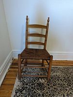 Front view of small wooden ladderback chair with woven seat, showing four horizontal back slats and turned finials on top of each post.