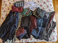 Full lot of men's clothing including pants, shirts, hoodie, and suit jacket laid out on floral bedspread