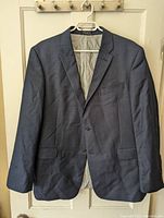Front view of navy blue sport coat with two-button closure hanging on a door.