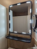 Rectangular black metal bathroom mirror mounted on wall with integrated shelf and LED lights installed along top, sides, and bottom.