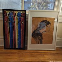 Two framed paintings leaning against a window: vertical colorful figures artwork and side profile portrait on tan background.