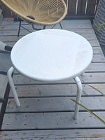 Photo of a round white outdoor table with a textured top and curved metal legs on a wooden deck with some dirt and debris on the surface.
