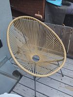 Photo showing a round patio chair with woven rope seat and metal frame on a wooden deck.
