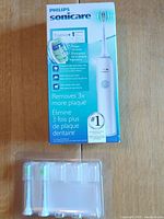 Photo of Philips Sonicare Essence+ electric toothbrush box with product image and features, along with two extra brush heads placed under the box.