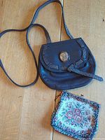 Black leather purse with flap, snake-textured trim and gold-tone circular accent on wooden surface