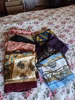 Various scarves laid on a floral bedspread, showing different patterns and colors including florals, geometric patterns, and animal print accents.
