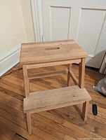 Photo showing wooden IKEA step stool with two steps in natural wood finish, positioned near door, surface slightly dirty.
