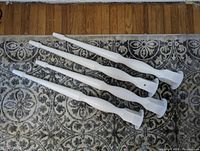 Four white wooden tapered table or desk legs with turned spindle design and flat square top, placed on decorative carpet background against wooden floor.