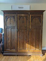 Front view of closed wardrobe showing three carved panel doors, decorative frieze and bun feet