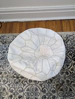 Top-down view of white leather Moroccan pouf cover showing stitched segmented design and visible wear.