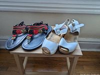 Pair of beaded sandals with multi-colored black, red, and gold detailing beside white leather strap wooden clogs on wooden bench