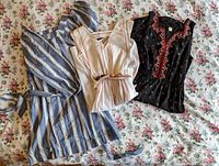 Three women's summer dresses laid out on floral sheet, blue/white stripes, off-white with stripes, black with red embroidery