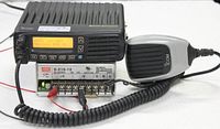 ICOM 2-way radio and microphone connected to Mean Well power supply with LEDs on, unit powered and display showing text and channel info.