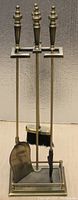 Full view of the brass fireplace tool set including poker, brush, shovel on stand.