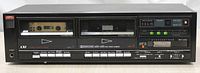 Front view of black LXI Model 28940 double cassette deck loaded with one cassette tape in the left compartment, showing buttons, meter display, and indicator lights.
