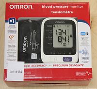 Front view of packaged Omron blood pressure monitor showing digital cuff device and branding with model number BP769CAN, displaying sample blood pressure reading on screen.