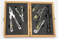 Wooden box open displaying four Sheffield multi-use tools and a mini Mag Lite flashlight set in black foam cutout inserts.