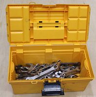 Open yellow toolbox showing assortment of metal hand tools mainly wrenches inside.