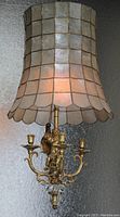 Side view of vintage capiz shell chandelier lit from inside, showing the translucent shell shade and ornate brass arms