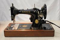 Side profile of vintage Singer sewing machine on wooden base showing the machine's body, handwheel, and accessory compartment.