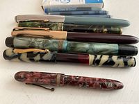 Six fountain pens laid out horizontally on white surface.