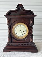 Front view of antique mahogany mantle clock showing detailed woodwork and clock face with Arabic numerals.