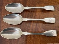 Top view of 3 antique sterling silver spoons arranged horizontally showing the bowl of each spoon and engraved initials on the end of the handles.