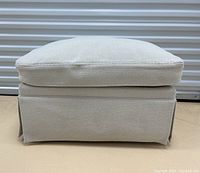 Front view of ottoman showing loose cushion top and skirted base