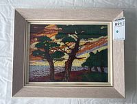 Framed needlepoint landscape showing full composition with two trees, water, and colorful sunset.