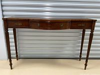 Frontal view of mahogany bow-front console table showing drawer and tapered legs.