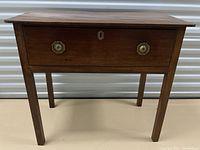 Front view of antique wooden side table showing single drawer with brass handles and keyhole.