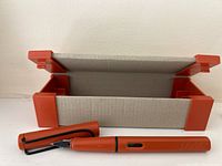 Orange Lamy Safari fountain pen with black clip and its box open showing the pen inside.