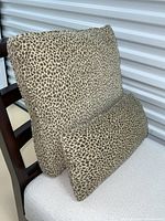 Two leopard print cushions displayed on a chair, one square and one cylindrical, showing the velvet fabric and pattern clearly.