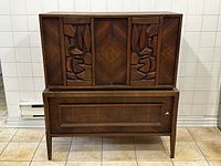 Front view of mid century walnut chest of drawers showing geometric carved design on top doors and three lower drawers.