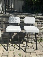 Photo of two modern gray upholstered swivel barstools with wooden legs and backrests, placed outside on stone patio