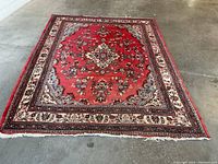 Full view of rug on concrete floor showing overall pattern, borders, and wear.