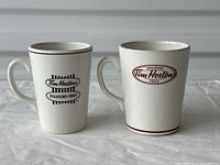 Pair of two Tim Hortons ceramic mugs, white with black logos and rims, showing overall good condition with some wear.