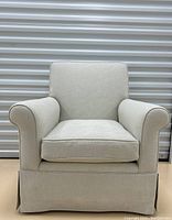 Front view of the upholstered armchair showing the light beige fabric, padded arms, cushioned back, and skirted base.