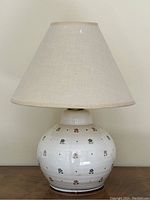 Side view of the assembled lamp with off-white ceramic base decorated with small colorful flowers and beige fabric lampshade