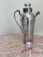 Full view of vintage chrome hammered cocktail shaker with 10 colorful glass fruit design skewers arranged on countertop.