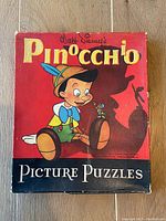 Closed image of red puzzle box featuring Pinocchio and Jiminy Cricket with some wear and rips on edges.