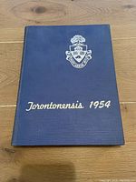 Hardcover front cover of 1954 Torontonensis yearbook in dark blue with University of Toronto crest and gold title text.