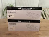 Two unopened boxes of black laser toner cartridges compatible with CRG104, stacked on a wooden table.