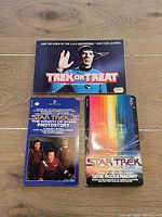 Three Star Trek books arranged on a wooden surface: 'Trek or Treat', 'Star Trek The Motion Picture', and 'Star Trek II The Wrath of Khan Photostory'.