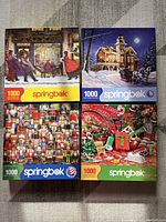 Four puzzle boxes arranged in two rows showing four different Christmas-themed scenes with 1000 pieces each by Springbok.