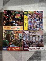 Four boxed Springbok jigsaw puzzles arranged in a 2x2 grid. Each box shows a colorful image related to sports and nostalgic collectibles, each puzzle has 1000 pieces.