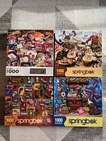 Four Springbok brand 1000-piece jigsaw puzzles, including one Hershey's themed, displayed laid flat on carpeted floor.