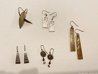 Five pairs of assorted earrings: metal leaf clip-ons, filigree rectangles, mother-of-pearl rectangles, silver-tone angular clip-ons, artistic round and swirl dangles with red beads.