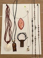 Eight necklaces arranged on a flat surface showing variety of pendants and materials such as wood, shell, beads, and metal.