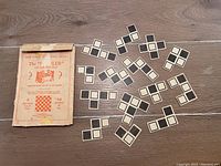 14 black and white square puzzle pieces scattered on a wood floor alongside the original box.